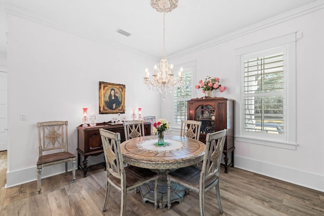 dining area with wood finished floors, visible vents, baseboards, crown molding, and a notable chandelier