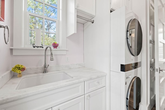 clothes washing area with cabinet space, stacked washer / drying machine, and a sink