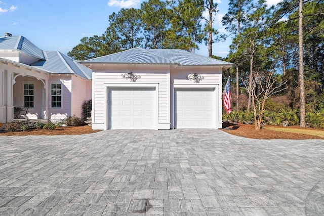 view of front of home featuring covered porch, metal roof, decorative driveway, a garage, and an outdoor structure