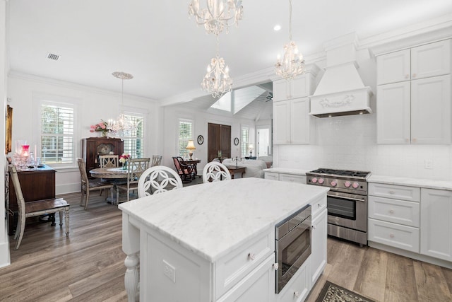 kitchen with stainless steel appliances, light wood finished floors, ornamental molding, and custom range hood