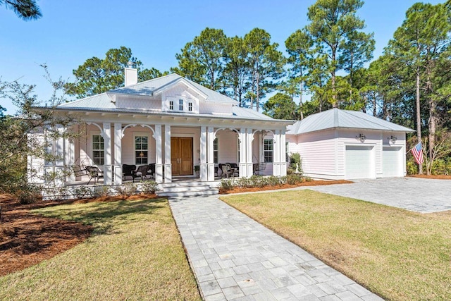 view of front of home featuring a porch, a chimney, a front lawn, an outdoor structure, and metal roof