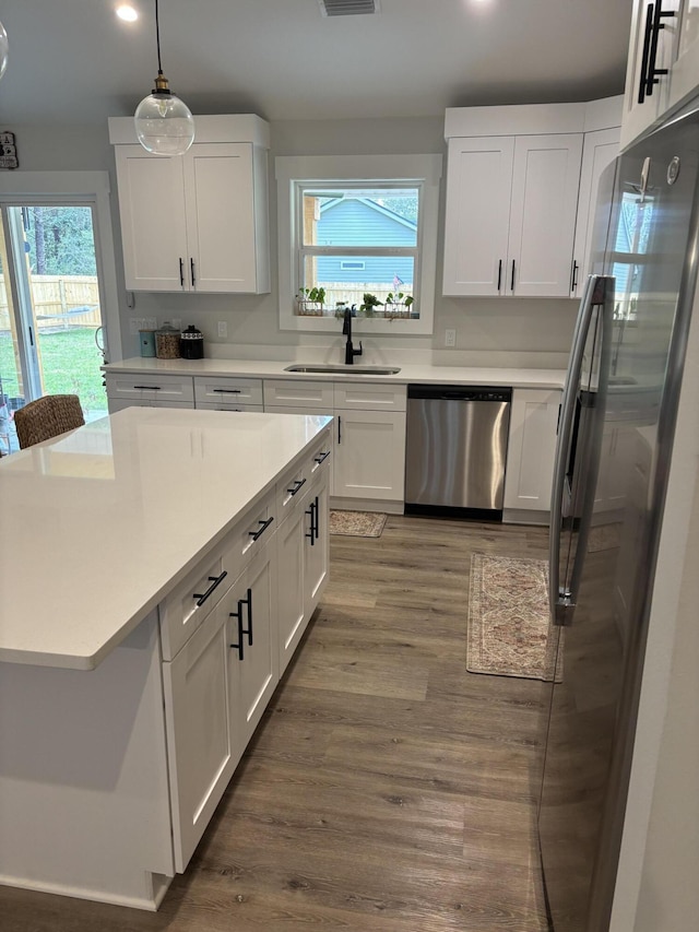 kitchen with a healthy amount of sunlight, stainless steel appliances, wood finished floors, white cabinetry, and a sink