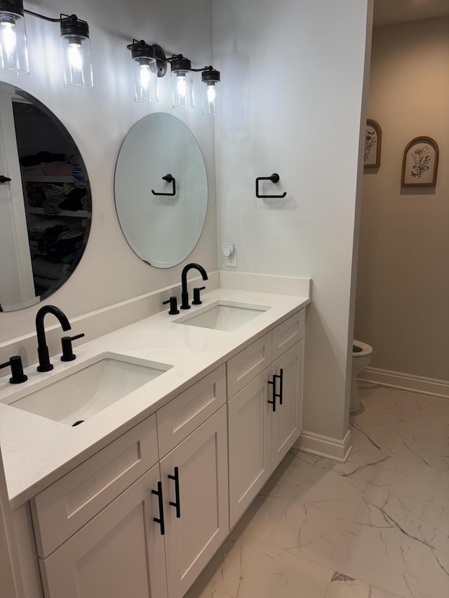 bathroom with a sink, baseboards, marble finish floor, and double vanity