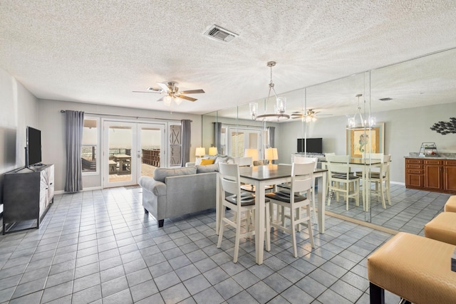 tiled dining area with visible vents, a textured ceiling, french doors, and ceiling fan with notable chandelier