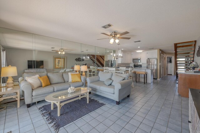 living room with light tile patterned floors, visible vents, ceiling fan with notable chandelier, and stairway