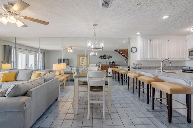 dining space featuring visible vents, french doors, light tile patterned flooring, a textured ceiling, and a ceiling fan