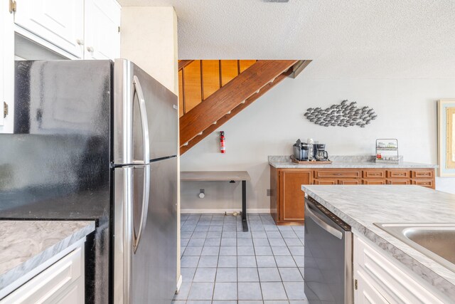 kitchen featuring light countertops, light tile patterned floors, appliances with stainless steel finishes, white cabinets, and a textured ceiling