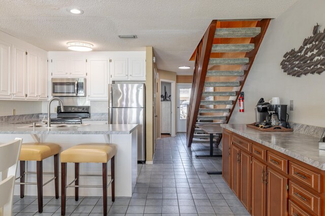 kitchen featuring visible vents, a breakfast bar, stainless steel appliances, white cabinetry, and a sink