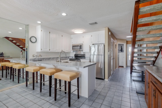 kitchen with visible vents, a sink, stainless steel appliances, a peninsula, and white cabinets