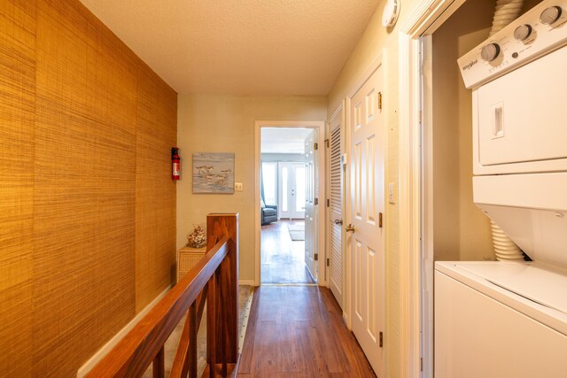 hall featuring dark wood-type flooring, stacked washer and dryer, and a textured ceiling