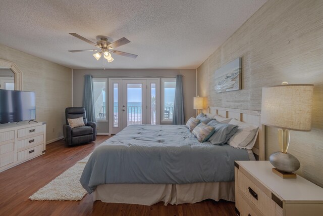 bedroom with a ceiling fan, a textured ceiling, wood finished floors, baseboards, and access to exterior