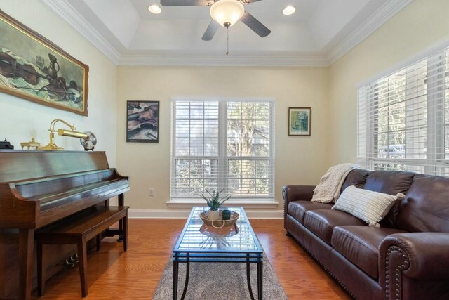 living room with baseboards, a tray ceiling, ornamental molding, wood finished floors, and a ceiling fan