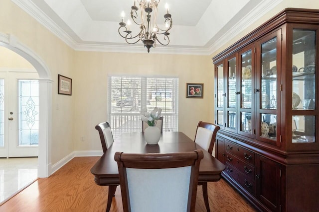 dining area featuring arched walkways, a notable chandelier, a tray ceiling, and wood finished floors