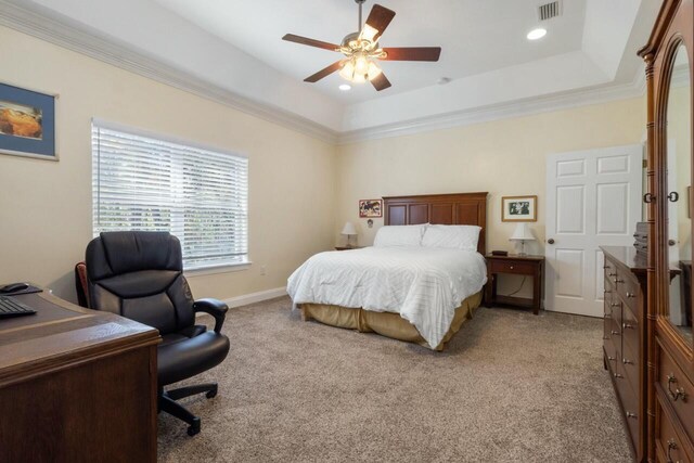 bedroom with visible vents, ceiling fan, light colored carpet, a tray ceiling, and ornamental molding