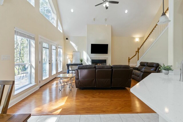 living room with a tiled fireplace, stairs, a high ceiling, wood finished floors, and a ceiling fan