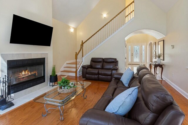 living area with a tiled fireplace, high vaulted ceiling, baseboards, and wood finished floors