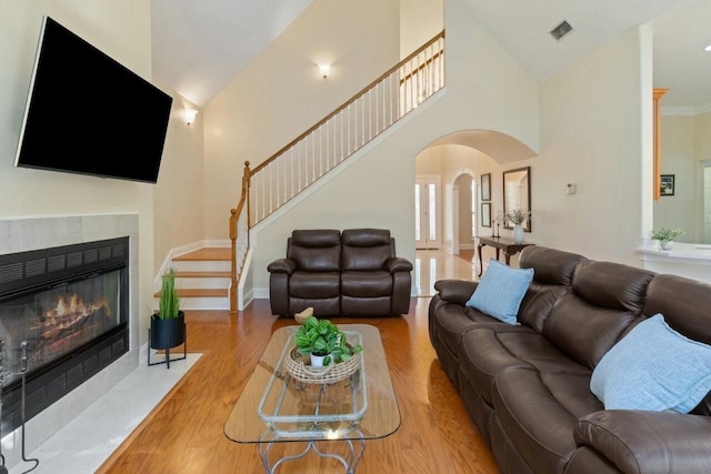 living area featuring visible vents, a tiled fireplace, stairs, wood finished floors, and arched walkways