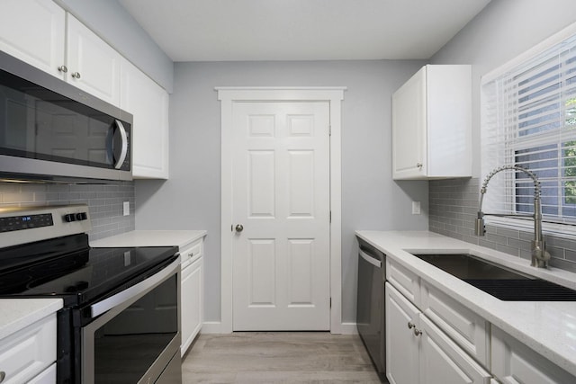 kitchen with light wood finished floors, light stone counters, white cabinets, stainless steel appliances, and a sink