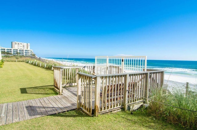 view of community with a deck with water view, a lawn, and a beach view