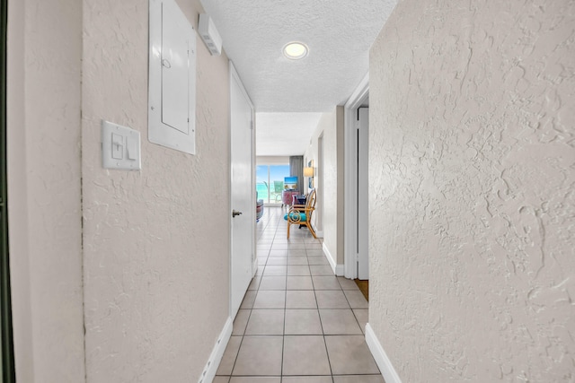 corridor with light tile patterned flooring, a textured ceiling, electric panel, baseboards, and a textured wall