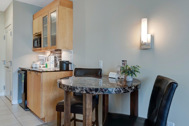 kitchen featuring backsplash, light brown cabinets, glass insert cabinets, a breakfast bar area, and light tile patterned flooring