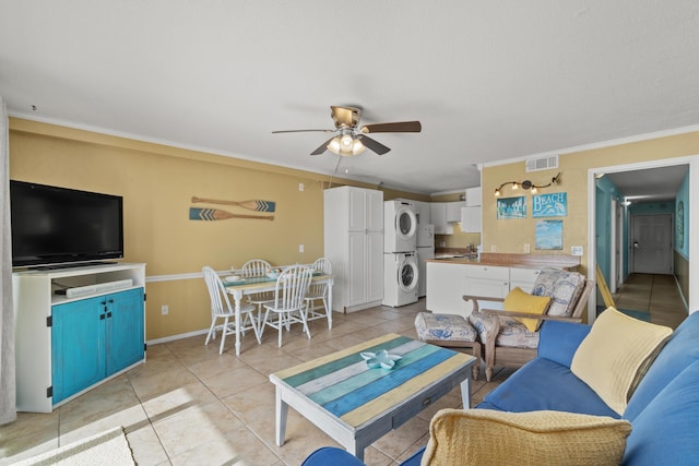 living room featuring visible vents, light tile patterned flooring, ceiling fan, crown molding, and stacked washer / dryer