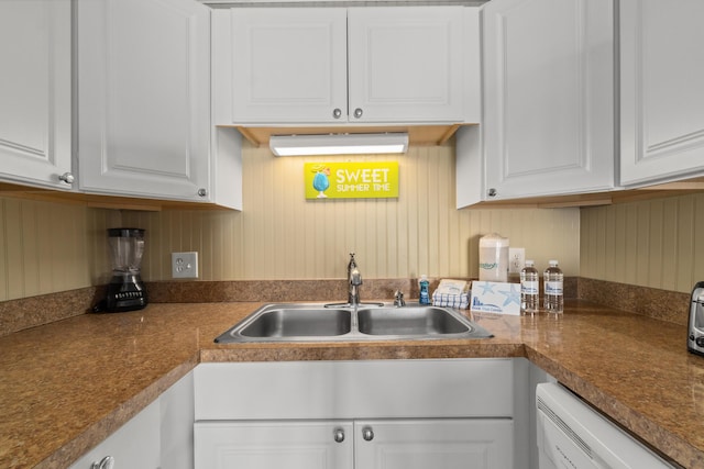 kitchen with dark countertops, white cabinets, white dishwasher, and a sink