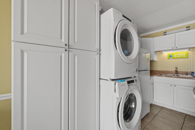 clothes washing area with stacked washer and dryer, light tile patterned floors, cabinet space, a textured ceiling, and a sink