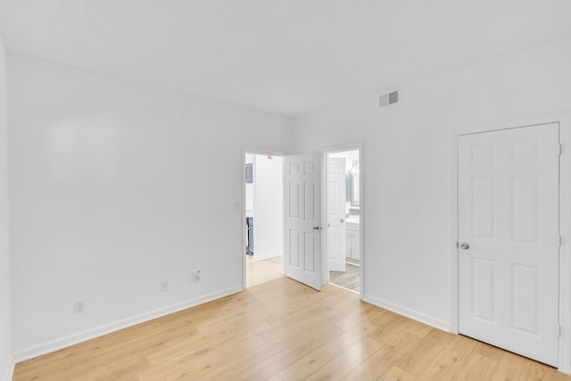 unfurnished bedroom with visible vents, light wood-style flooring, connected bathroom, and baseboards