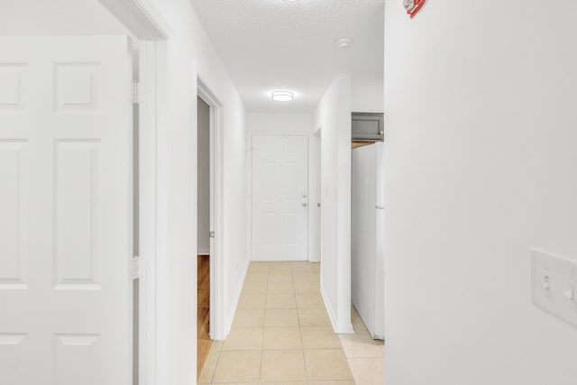 corridor featuring light tile patterned floors, a textured ceiling, and baseboards