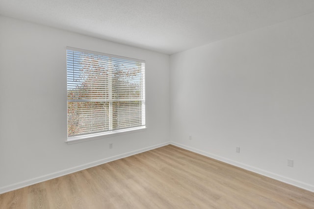 empty room featuring a textured ceiling, baseboards, and light wood-style floors