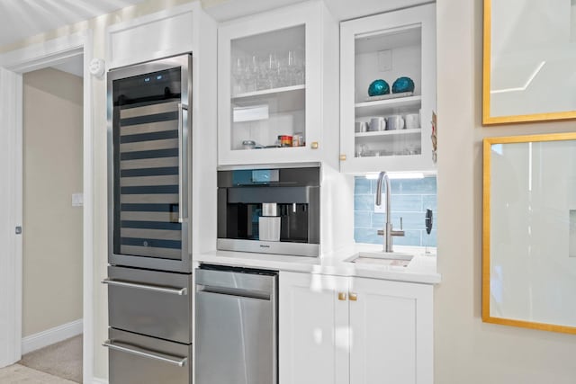 kitchen with glass insert cabinets, beverage cooler, light countertops, white cabinets, and a sink