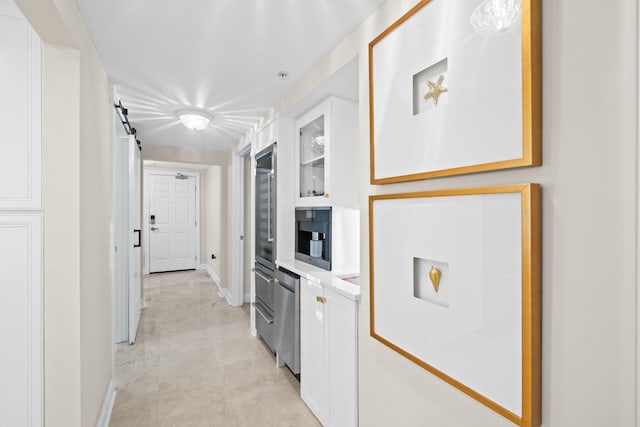 kitchen featuring baseboards, light countertops, glass insert cabinets, white cabinetry, and a barn door