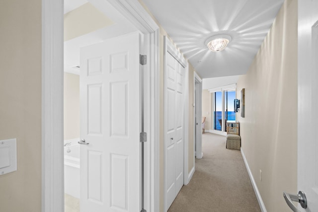 hallway featuring light carpet and baseboards