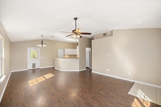 unfurnished living room featuring visible vents, baseboards, vaulted ceiling, ceiling fan with notable chandelier, and dark wood-style flooring