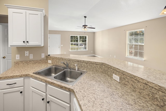 kitchen with a peninsula, ceiling fan, a sink, light countertops, and white cabinets