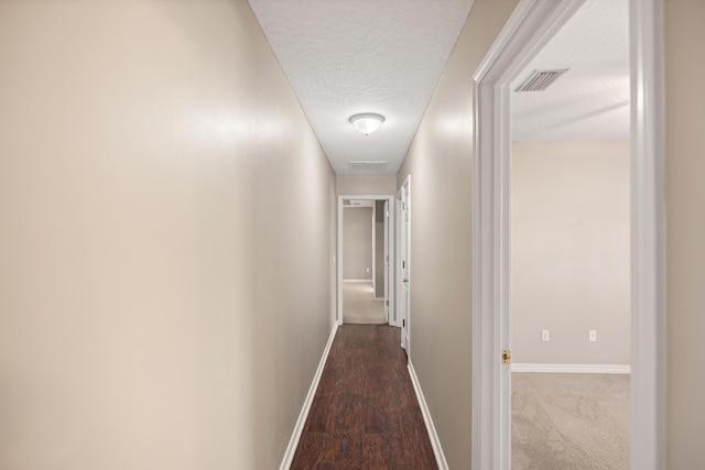 hall with visible vents, a textured ceiling, baseboards, and wood finished floors