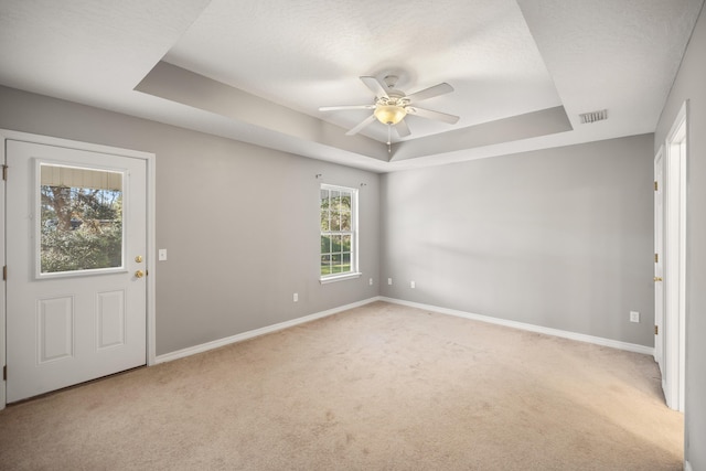 spare room with a tray ceiling, visible vents, baseboards, and carpet floors