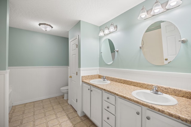 full bath featuring a sink, a textured ceiling, wainscoting, and tile patterned floors