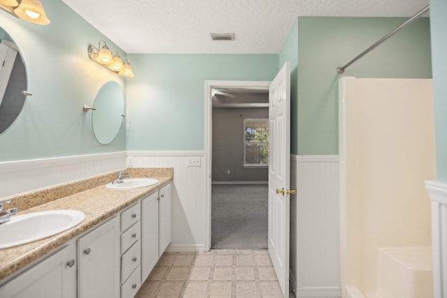 full bathroom featuring visible vents, wainscoting, a textured ceiling, and a sink