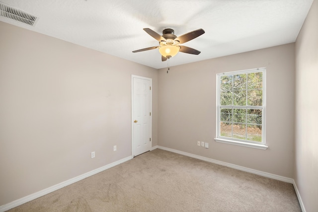 empty room with light carpet, visible vents, a ceiling fan, and baseboards