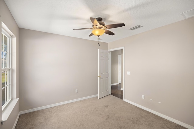 empty room featuring visible vents, baseboards, ceiling fan, light colored carpet, and a textured ceiling