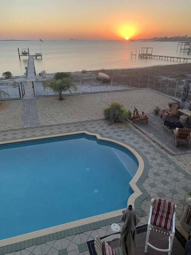 pool at dusk with a fenced in pool, fence, and a water view