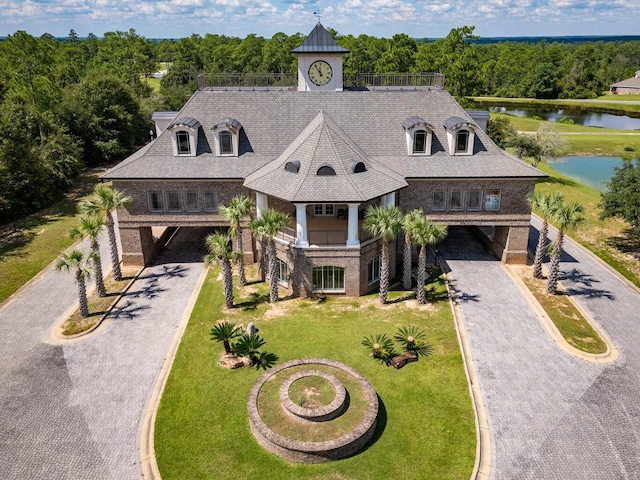 view of front of home with a water view, driveway, a view of trees, a front yard, and brick siding