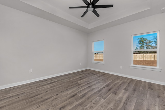 spare room with a tray ceiling, a ceiling fan, baseboards, and dark wood-style flooring