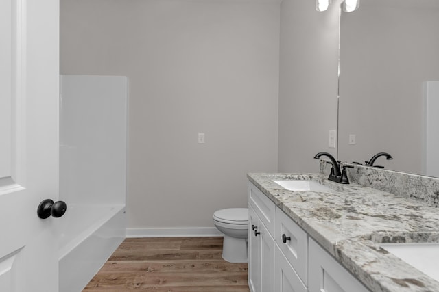 full bathroom featuring wood finished floors, baseboards, double vanity, a sink, and toilet