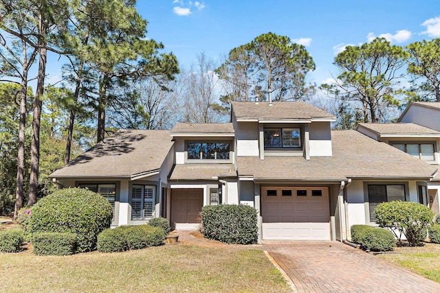 view of front of property featuring a front yard, a shingled roof, stucco siding, a garage, and decorative driveway