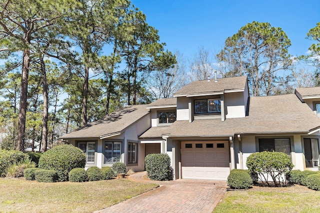 view of front facade with stucco siding, decorative driveway, a front yard, and an attached garage