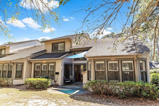 rear view of property featuring a shingled roof, a patio area, and stucco siding