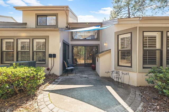 entrance to property featuring central AC unit, a patio area, and stucco siding